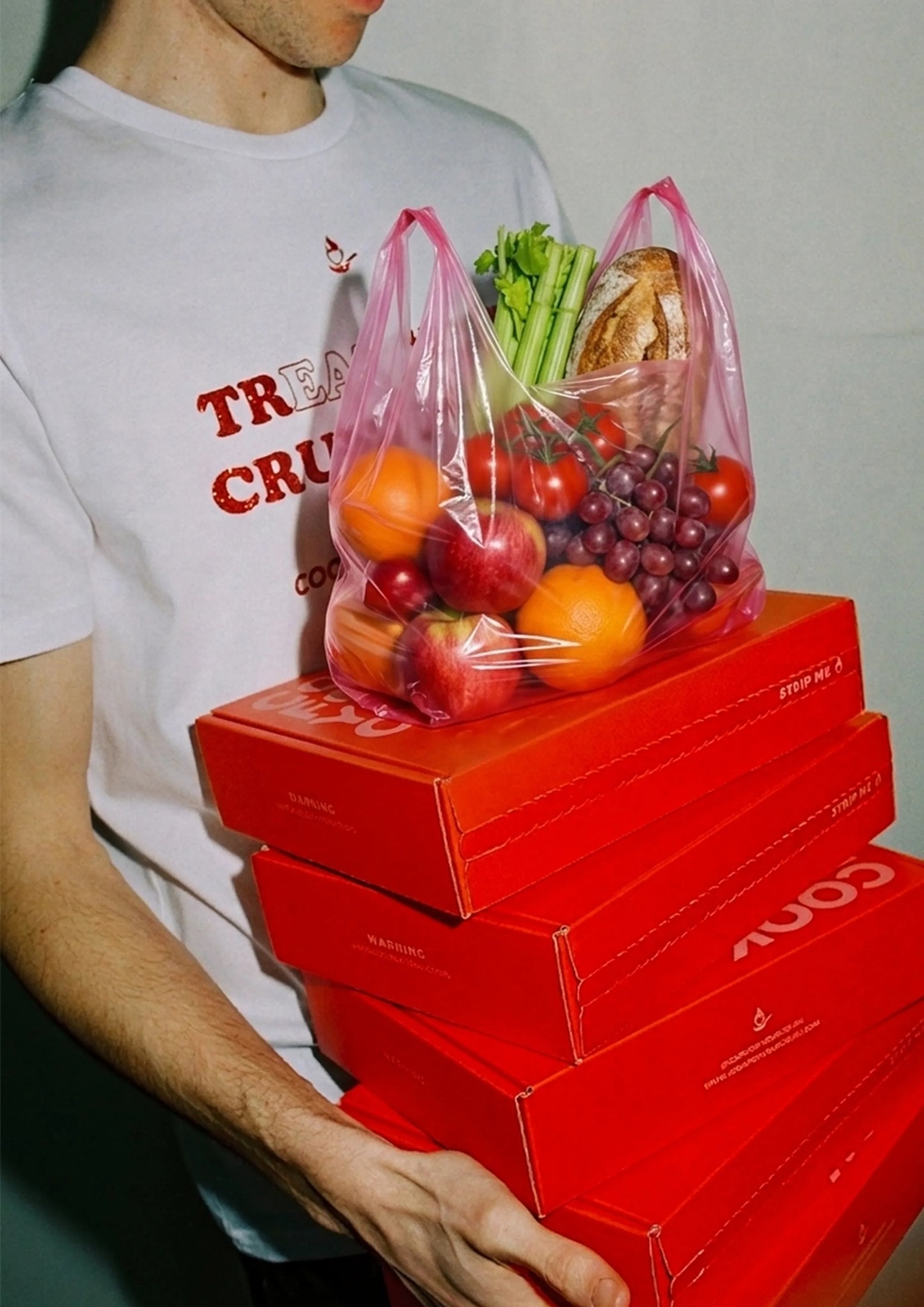 Man holding a tall stack of red Cook For Your Crush date night boxes and a pink bag with fresh produce, bread, and fruits